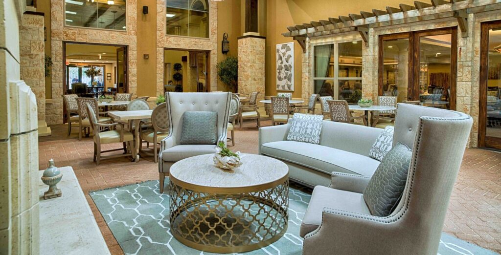 Large chandeliers hang over seating and a fireplace in a common room at The Landon at Lake Highlands, a Forest Hills senior living option.