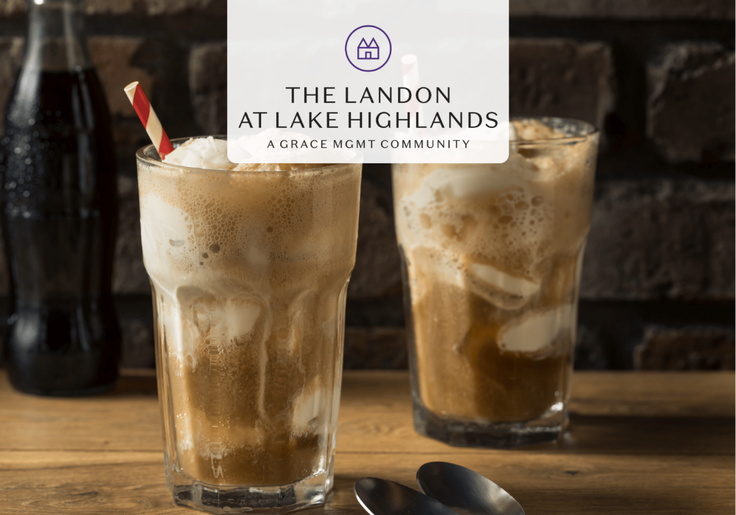 Two tall glasses of iced coffee with red-and-cream striped straw on a wooden table, foam on top, brick wall background; overlay reads 'The Landon at Lake Highlands' with a circular logo.